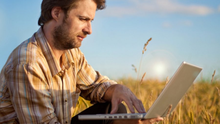 Ein Landwirt steht mit einem geöffneten Laptop vor einem reifen Weizenfeld